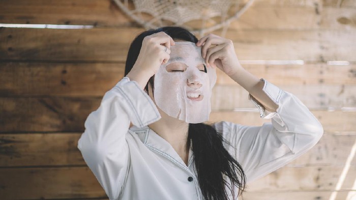 Mature women home in pajama spending cozy morning during isolation period. She wearing sheet mask and have video call, her dog is in bed too