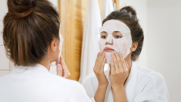 Mature women home in pajama spending cozy morning during isolation period. She wearing sheet mask and have video call, her dog is in bed too