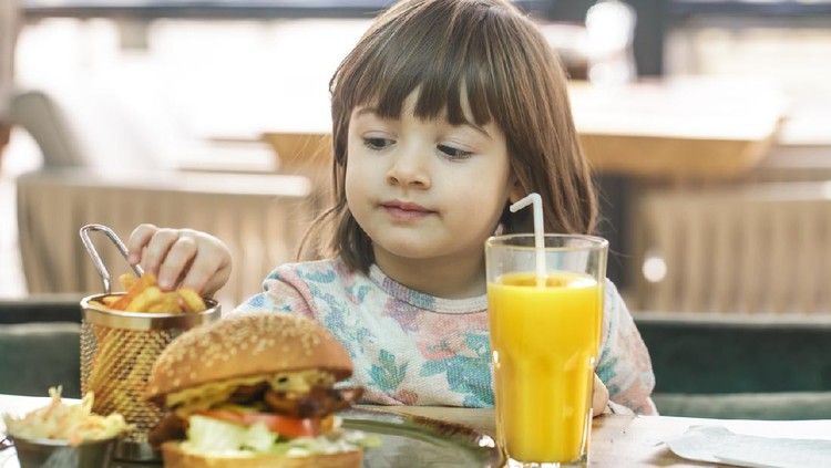 fast food Little cute girl eating a fast food sandwich with fries and orange juice in a cafe. Fast food concept.