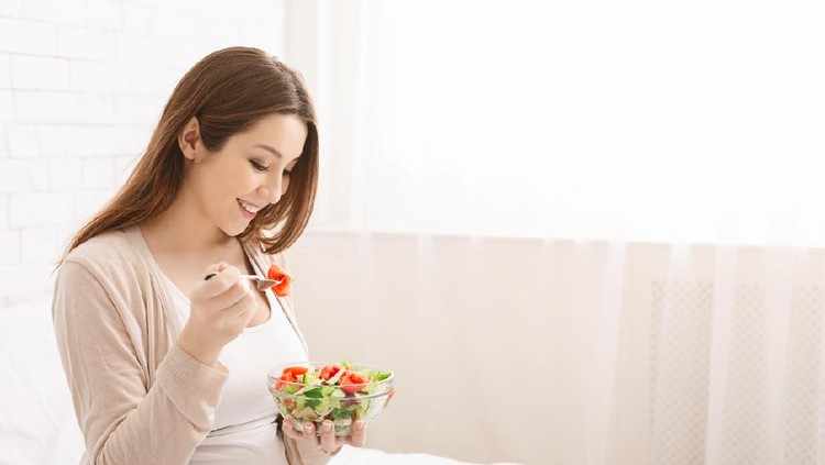 Healthy organic nutrition. Pregnant millennial woman eating natural vegetable salad in bed, empty space