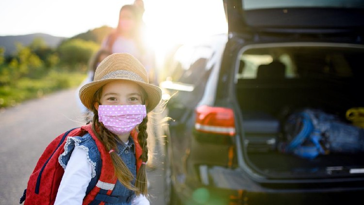 Front view of small girl with family on trip outdoors in nature, wearing face masks.