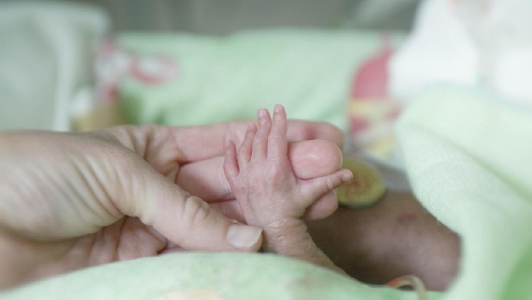 A mother holds the tiny hand of her premature baby in hospital