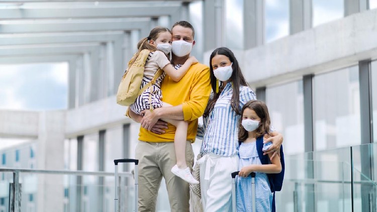 Happy family with two children going on holiday, wearing face masks at the airport.