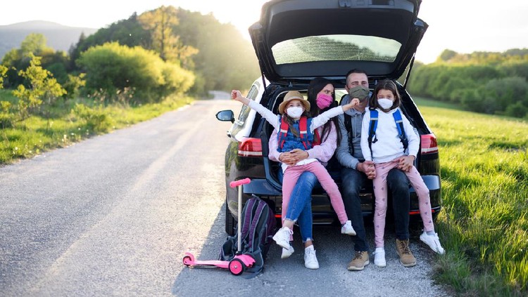 Front view of family with two small daughters on trip outdoors in nature, wearing face masks.