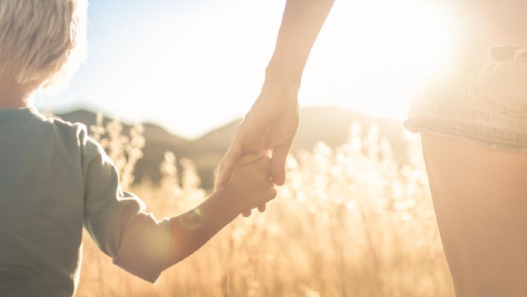 Mother and son holding hands walking at sunset.