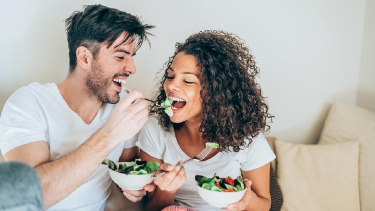 Happy man feeding his girlfriend with salad