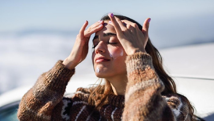 Young woman applying sunscreen on her face in snowy mountains in winter, in Sierra Nevada, Granada, Spain. Female wearing winter clothes.