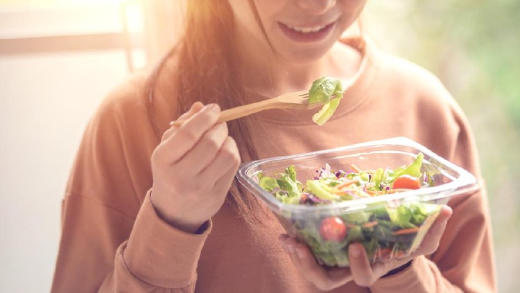 closeup woman eating healthy food salad, focus on salad and fork