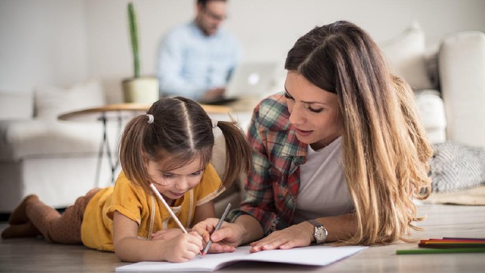 Getting help with my tasks. Little girl working her homework with mother. Focus is on foreground.
