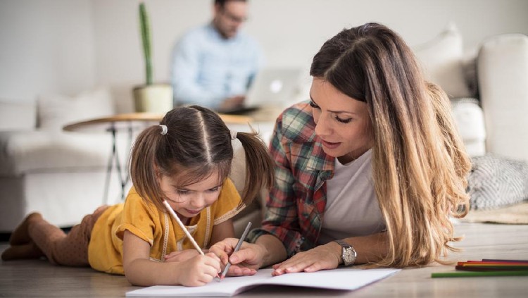 Getting help with my tasks. Little girl working her homework with mother. Focus is on foreground.