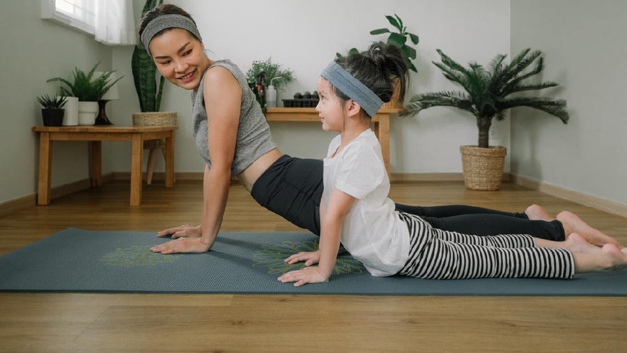 Asian little girl and her mother enjoying free time at home in the living room, practicing yoga together.