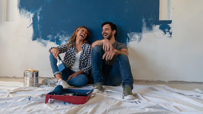 Portrait of a happy couple laughing while taking a break from painting - home improvement concepts