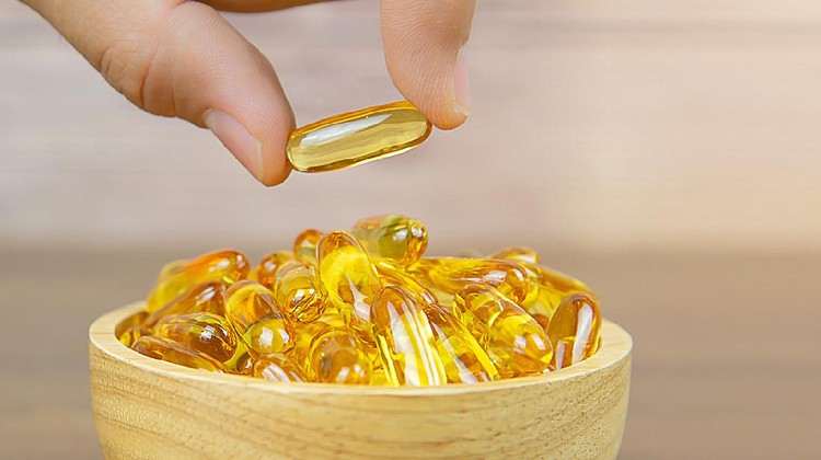 vitamin d Hand picked cod liver oil capsule or fish oil in a wooden cup. Dietary supplement for health-care concepts.