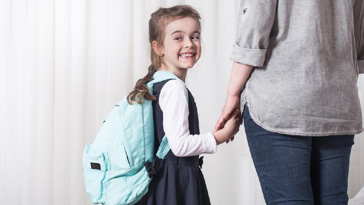 Parent and elementary school student go hand in hand on a light background . Back to school concept