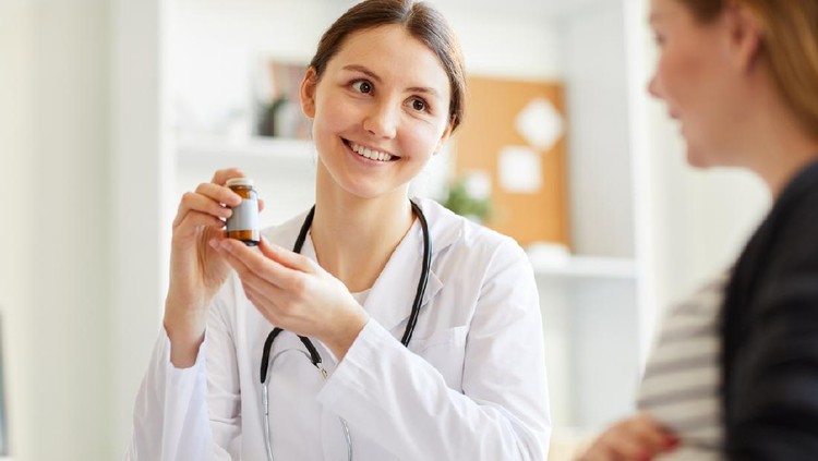 Portrait of smiling female obstetrician showing vitamins to pregnant woman during consultation in parenthood clinic, copy space