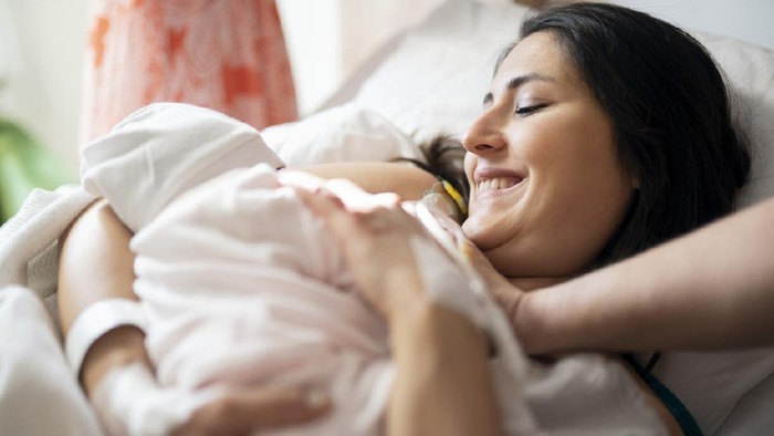 Mother breastfeeding newborn baby in hospital ward, first breastfeeding