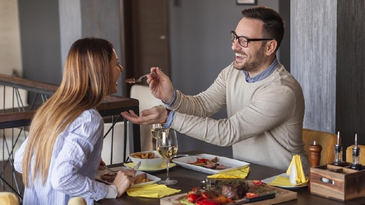 Couple eating lunch at a restaurant, tasting each other's food and having fun
