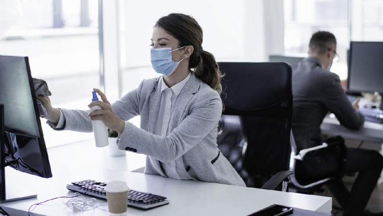 Businesswoman disinfecting monitor in office. Covid-19