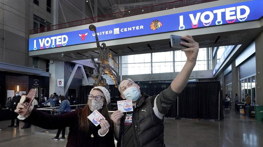 Samantha Jones, left, and Peter Vina take selfies near the Michael Jordan statue on Election Day, Tuesday, Nov. 3, 2020, in the atrium of the United Center, transformed into a super voting site in Chicago. (AP Photo/Charles Rex Arbogast)