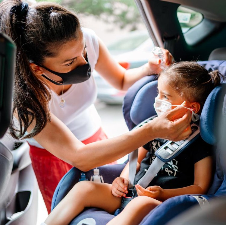Liburan saat Corona Portrait of a mother fastening her daughter safely in a car seat