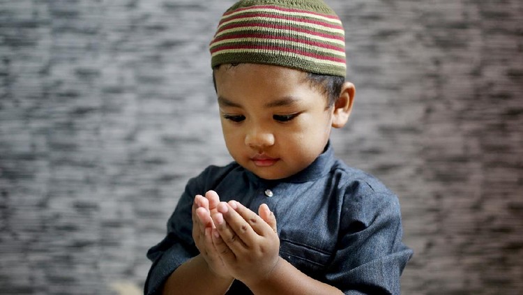 A Muslim young man is putting both palms together (Muslim way of praying) at home in Malaysia. He is wearing 'baju Melayu', a traditional Muslim menswear.