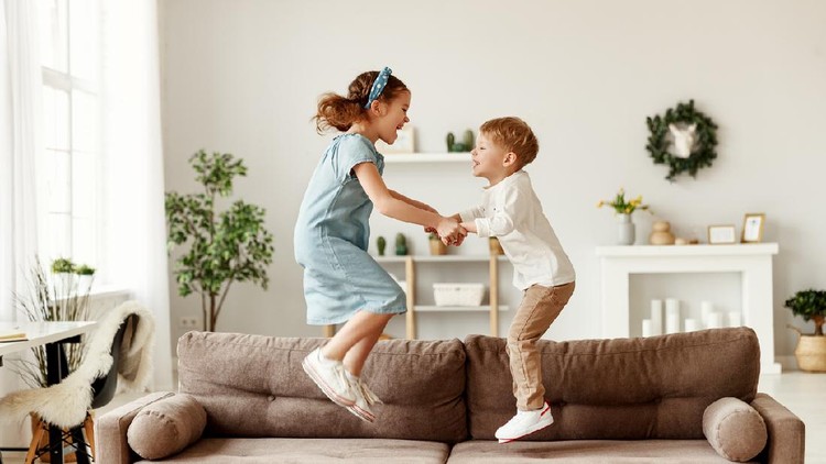 anak main Side view of cheerful boy and girl holding hands and jumping on couch while having fun at home together