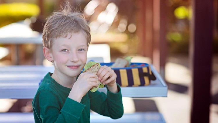beautiful positive schoolboy enjoying healthy lunch during recess outdoor