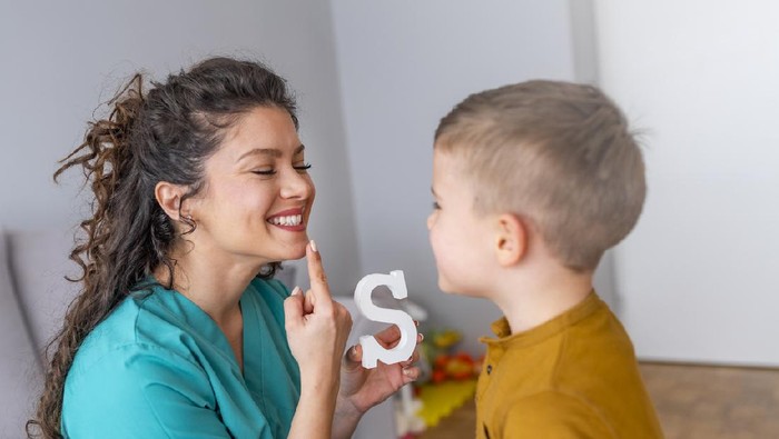 Cute little boy at speech therapist office. Shot of a speech therapist during a session with a little boy. Boy and young woman teacher during private home lesson