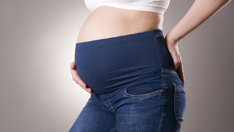 Pregnant woman in blue jeans with high waist on gray background