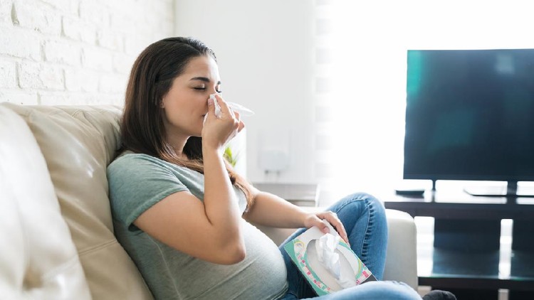 Beautiful expectant female feeling sick at home and blowing her nose with a tissue