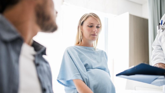 Doctor explaining medical records to pregnant woman sitting with man. Male professional is discussing with mid adult couple. They are in hospital ward.