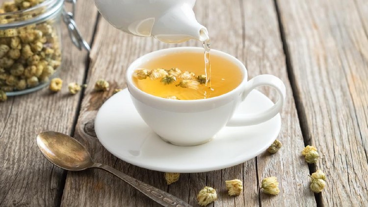 Teh chamomile Healthy chamomile tea poured into white cup. Teapot and spoon, glass jar of daisy medicinal herbs.