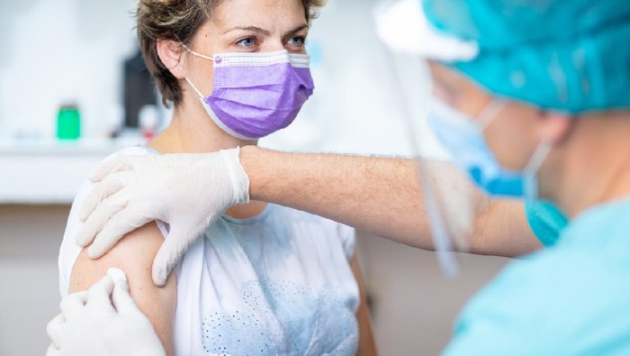 Female patient with protective face mask waiting for vaccination, doctor in surgical gloves disinfecting her arm