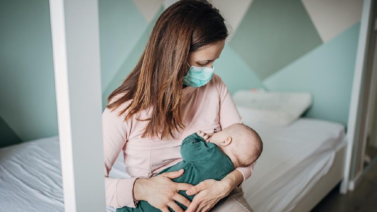 Menyusui Two people, mother with protective mask breastfeeding her baby son at home, they are at home do to pandemic outbreak quarantine.