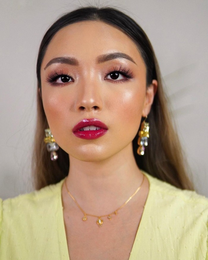 Melalui channel Youtube-nya, beauty vlogger Gel Angelica membagikan tutorial glossy makeup look yang terkesan glam dengan sentuhan lipstik merah. Untuk mendapatkan look ini, ia menggunakan glossy eyeshadow dan foundation yang dewy, serta highlighter di tulang pipi, hidung, dagu hingga inner corner. Penampilannya semakin glossy dengan sentuhan lipgloss berwarna rosy red yang juga memberi efek bibir plumpy. (Foto: instagram.com/gelangelicca)
