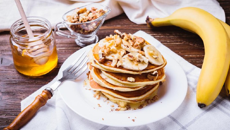 Pancakes with banana, walnuts and honey. Healthy breakfast. On dark wooden table background.