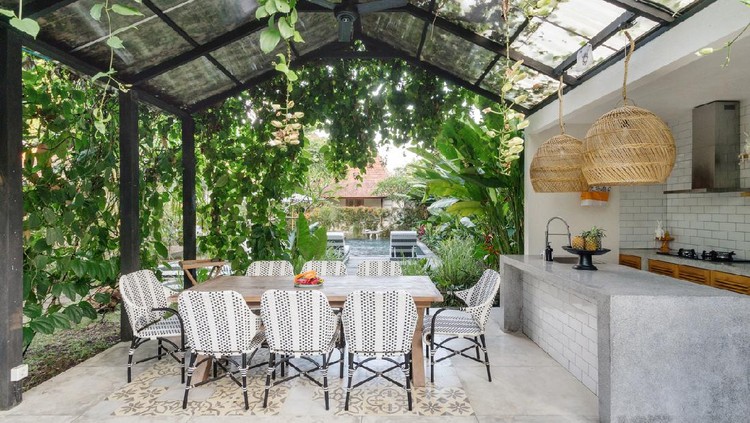 Open kitchen with empty dining room table and chairs outside, against green fresh plants on background
