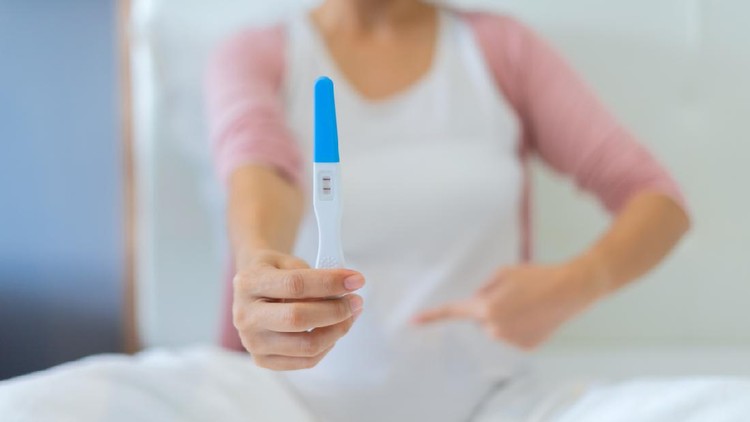 Tes Kehamilan Close up of woman hand holding a positive home pregnancy test in bedroom at home
