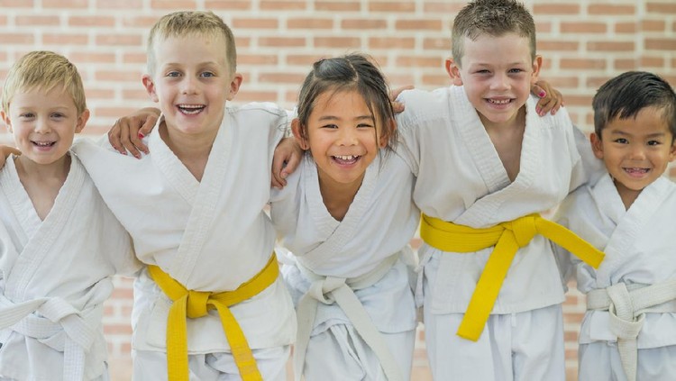 649037434 A group of elementary age children are taking a martial arts class. They are standing together in a row and are smiling while looking at the camera.
