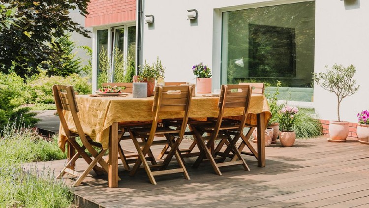 Dining table covered with orange tablecloth standing on wooden terrace in green garden