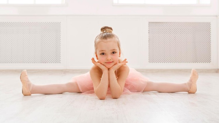 Little ballerina in split on floor, copy space. Smiling baby girl dreaming to become professional ballet dancer, classical dance school