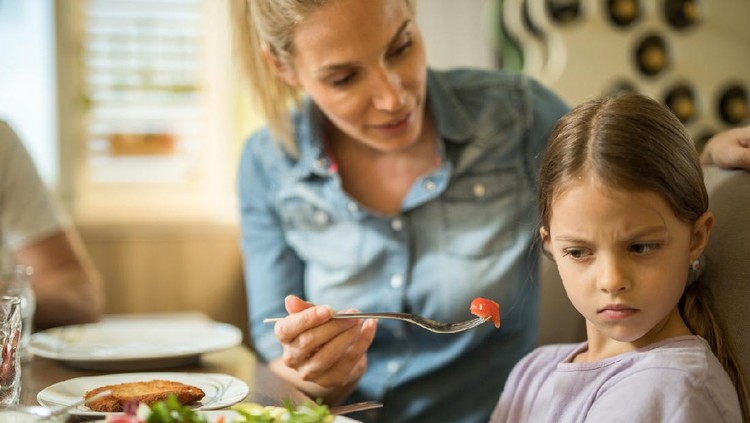 Anak makan Displeased girl refusing to eat cherry tomato while her mother is feeding her.