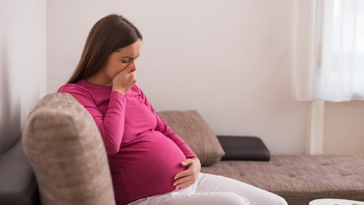 Pregnant woman feels sick while while sitting on sofa at her home.