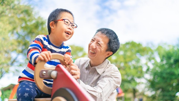 A small child with down syndrome is enjoying with his father at a public park on a sunny day.