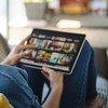Caucasian woman lying down on sofa in living room at home searching for film or TV series to watch for leisure on her tablet.