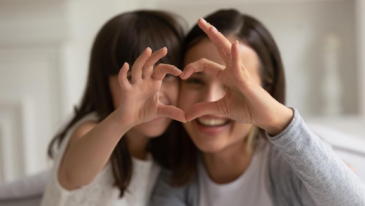 Happy young mother with cute little daughter making focused heart sign with hands, looking at camera. Smiling millennial mom and small girl showing love gesture together, expressing care, affection.