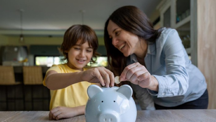 Sweet mother and son inserting coins into a piggy bank at home both smiling