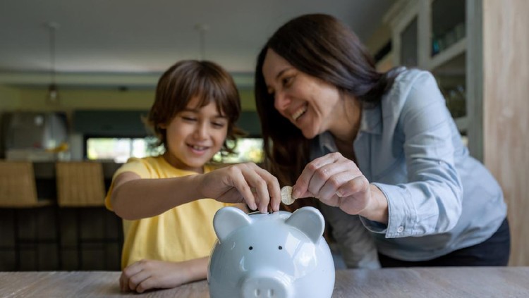 Sweet mother and son inserting coins into a piggy bank at home both smiling