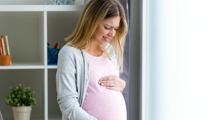 Shot of pregnant young woman feels pain and stomachache and touching her belly at home