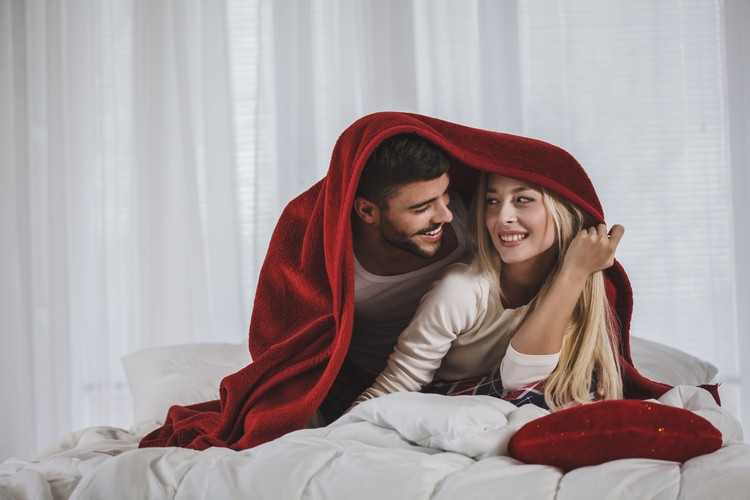 ilustrasi seks Front view of happy young couple in pajamas decided to have fun by playing under red blanket during long days of quarantine at home.